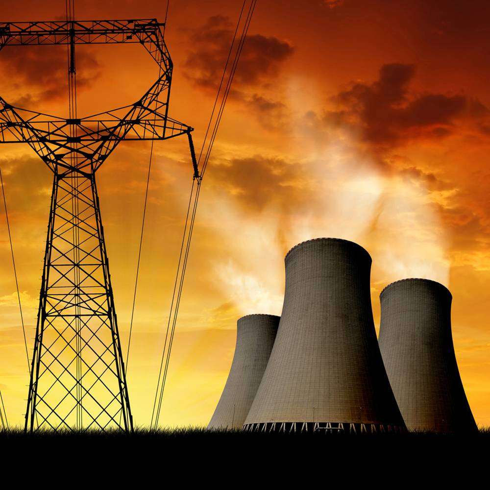 Nuclear power plants and power lines silhouetted against a vibrant sunset